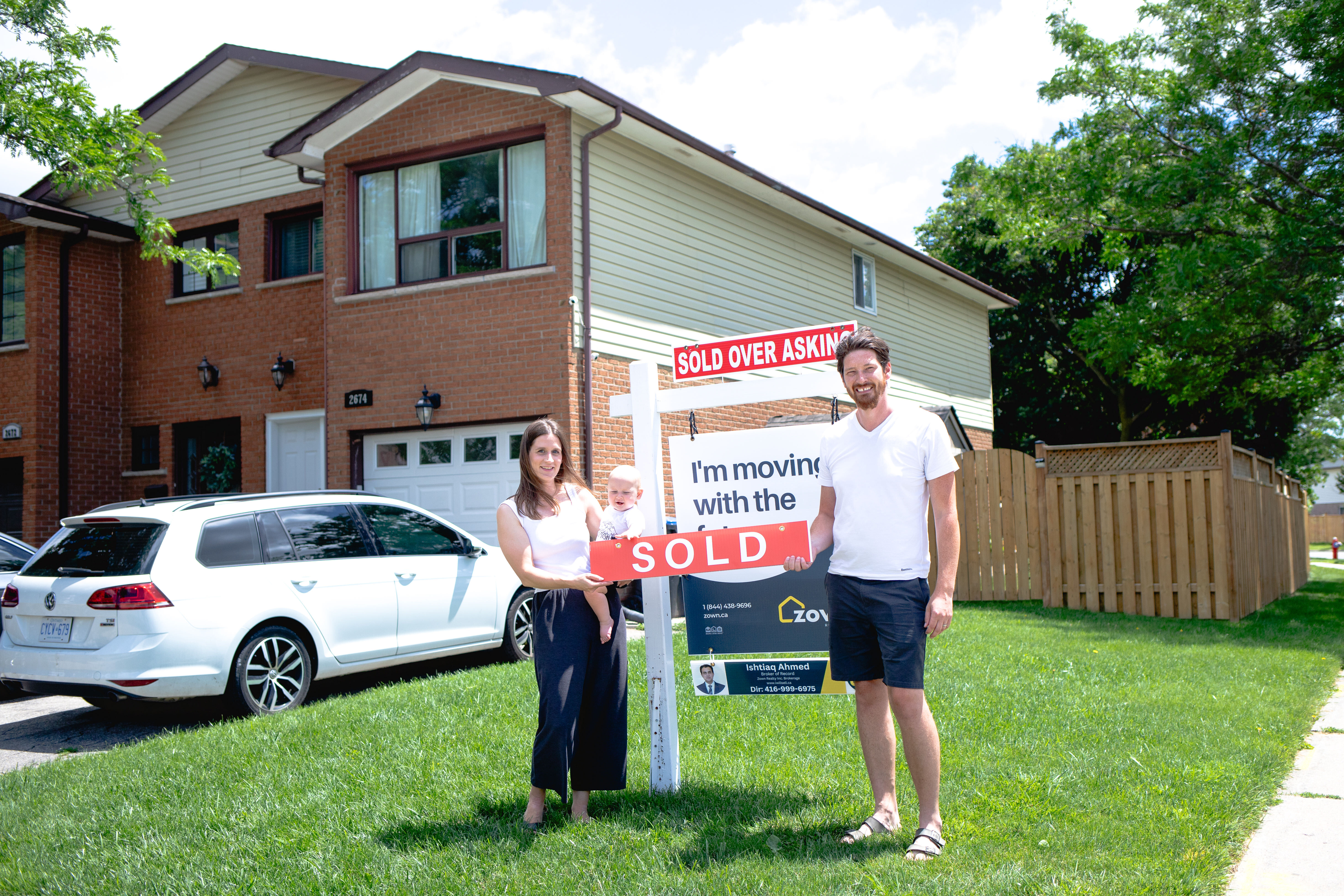 A family standing in front of their home with a sold sign and Zown signage.